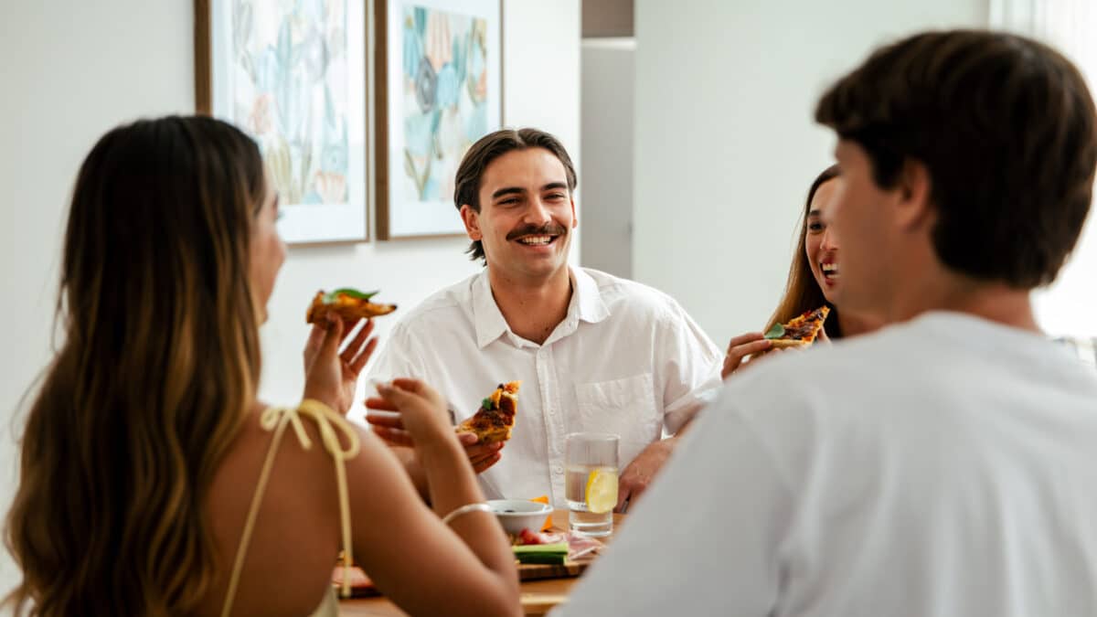 First home buyer sit together with their friends at the dining table. The home design features open plan living spaces that is light and bright. This modern home is built by Step 1 Homes.