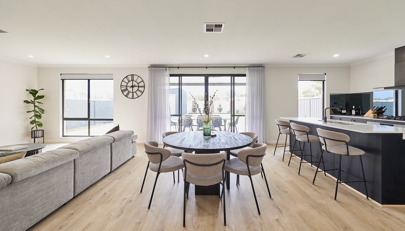 This spacious first-home buyer home design features qualiy specifications and inclusions, including an open plan living space, with large windows that let in natural light. There is a round dark wooden dining table in the centre of the rooms, that is complemented by the dark wood of the kitchen island benches and kitchen cabinetry. This modern first home is perfect for first home buyers who love to entertain with the view of the outdoor alfresco from the living, dining, and kitchen.